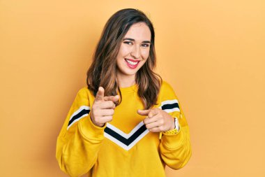 Günlük kıyafetler giyen genç İspanyol kız mutlu ve komik yüzüyle kamerayı işaret ediyor. iyi enerji ve titreşimler. 