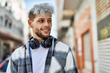 Şehirde kulaklık takarak mutlu gülümseyen genç İspanyol adam..