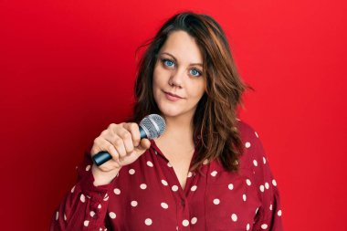 Genç beyaz kadın mikrofon kullanarak şarkı söylüyor. Düşünme tavrı takınıyor ve ayık ifadesi takınıyor. Kendine güveniyor gibi görünüyor. 