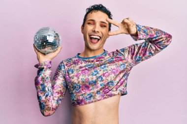 Handsome man wearing make up holding shiny disco ball smiling and laughing hard out loud because funny crazy joke. 