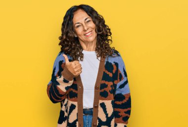 Orta yaşlı İspanyol kadın gündelik giysiler giyip mutlu mesut el hareketi yapıyor. Kameraya bakıp başarıyı gösteren ifade. 