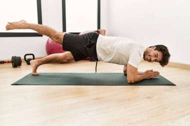 Genç İspanyol adam gülümsüyor spor merkezinde kendine güvenen karın kasları egzersizi yapıyor.