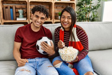 Evdeki kanepede oturan genç latin çift futbol maçını izliyor ve destekliyor..