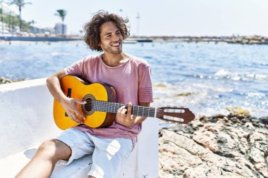 Genç İspanyol adam klasik gitar çalıyor sahildeki bankta oturuyor..