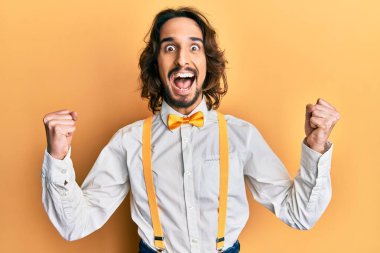 Hipster tarzı şık giyinen genç İspanyol adam kollarını kaldırıp, gözlerini açarak başarıyı kutluyor ve şaşırıyor. Kazanan konsept. 