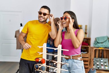 Genç Latin çift gülümseyerek mağazadan güneş gözlüğü seçiyor..