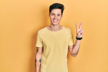 Gündelik sarı tişört giyen genç İspanyol adam iki numarayı gösterip işaret ederken kendinden emin ve mutlu gülümsüyor.. 