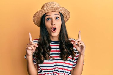 Yaz şapkası takan genç İspanyol kadın şaşırdı ve şaşırdı. Yukarı baktı ve parmaklarıyla işaret etti ve kollarını kaldırdı.. 