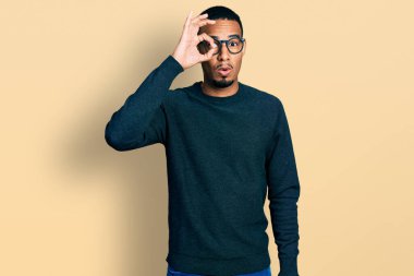 Sıradan kıyafetler ve gözlük takan Afro-Amerikan genç adam şaşırmış yüz ifadesiyle şaşırmış ve parmaklarından içeri bakıyordu. İnançsız ifade. 