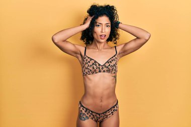 Genç Latin kız bikini giyiyor çılgın ve elleri başının üstünde korkmuş, şokdan korkmuş ve ağzı açık. 