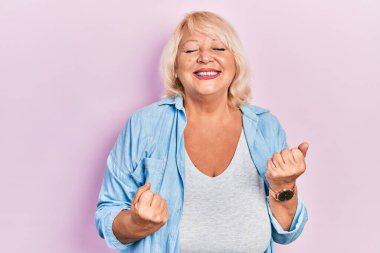 Orta yaşlı, sıradan kıyafetler giyen, mutlu ve heyecanlı kolları havada, gülümseyen ve başarı için bağıran, kazanan bir jest yapan orta yaşlı bir kadın. kutlama konsepti. 