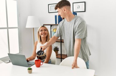 Kadın evde dizüstü bilgisayar kullanıyor ve erkek arkadaşı kahve dolduruyor..