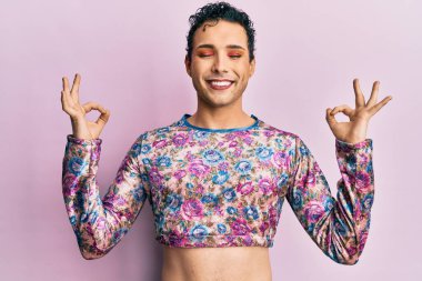 Handsome man wearing make up wearing fashion clothes relax and smiling with eyes closed doing meditation gesture with fingers. yoga concept. 