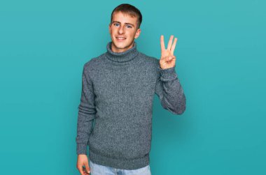 Gündelik kıyafetler giyen genç sarışın üç numarayı gösterip işaret ederken kendinden emin ve mutlu bir şekilde gülümsüyor.. 