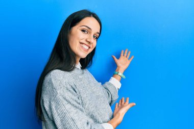 Gündelik kıyafetler giyen genç İspanyol kadın gülümseyerek doğal bir şekilde içeri girmeye davet ediyor. 