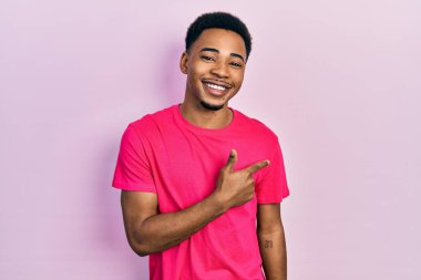 Young african american man wearing casua t shirt cheerful with a smile of face pointing with hand and finger up to the side with happy and natural expression on face 
