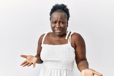 Beyaz soyutlanmış arka planda duran Afrikalı genç bir kadın. Hiçbir fikri olmayan, kolları açık bir şekilde kafası karışmış.. 