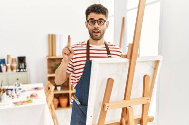 Arab young man at art studio pointing finger up with successful idea. exited and happy. number one. 