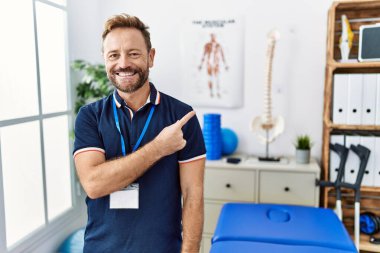 Orta yaşlı fizyoterapist. Ağrı giderme kliniğinde çalışıyor. Yüzünde mutlu ve doğal bir ifadeyle gülümseyen bir yüz ifadesi var. 