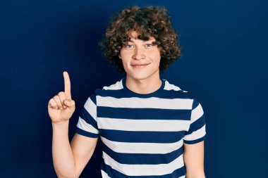 Handsome young man wearing casual striped t shirt showing and pointing up with finger number one while smiling confident and happy. 