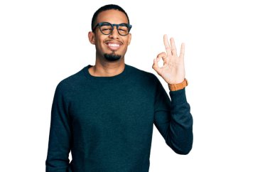Sıradan kıyafetler ve gözlüklerle gülümseyen Afro-Amerikalı genç adam el ve parmaklarıyla 