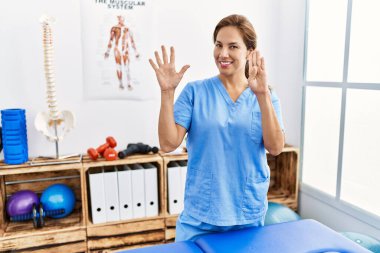 Orta yaşlı İspanyol fizyoterapist kadın ağrı kesici kliniğinde çalışıyor. 9 numarayı gösterip işaret ederken kendine güveni tam ve mutlu.. 