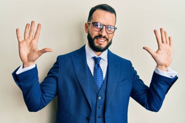 Sakallı, takım elbiseli ve kravatlı genç adam on numarayı gösterip işaret ederken kendinden emin ve mutlu gülümsüyor.. 