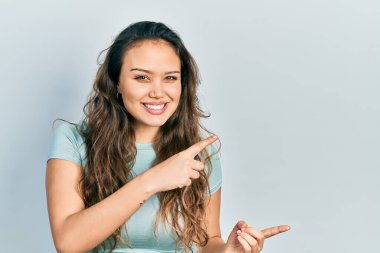 Gündelik tişört giyen genç İspanyol kız gülümseyip kameraya bakıyor ve iki eliyle ve parmaklarıyla kenarı işaret ediyor.. 