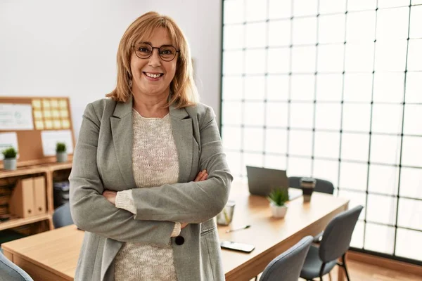 Middle age businesswoman smiling happy standing with arms crossed gesture at the office.