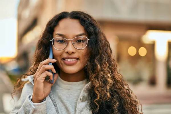Genç Latin kadın gülümsüyor. Şehirdeki akıllı telefondan konuşuyor..