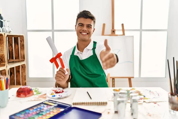 Young Hispanic Man Art Studio Holding Degree Smiling Friendly Offering — Fotografia de Stock