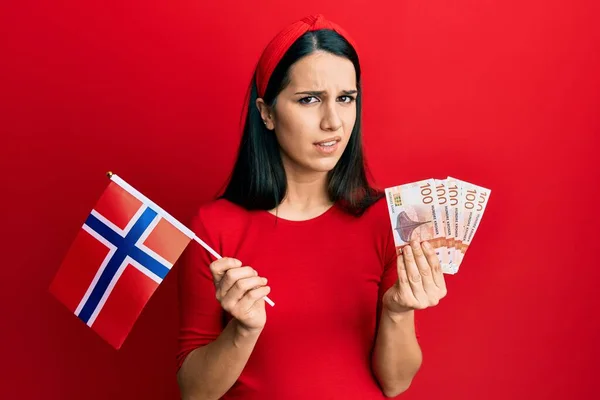 Молода Іспаномовна Жінка Тримає Прапор Норвегії Банкноти Крони Безглуздо Збентежений — стокове фото