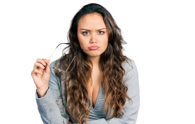 Young hispanic girl wearing business clothes holding glasses skeptic and nervous, frowning upset because of problem. negative person.  clipart