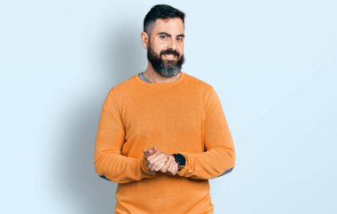 Hispanic man with beard wearing casual winter sweater with hands together and crossed fingers smiling relaxed and cheerful. success and optimistic 