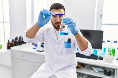 Genç İspanyol adam bilim adamı üniforması giyiyor. Laboratuvarda sıvı karıştırıyor.