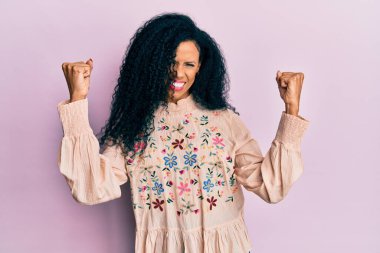 Orta yaşlı Afro-Amerikalı kadın gündelik kıyafetler giyip gururla bağırıyor zaferi ve başarıyı kutluyor. 