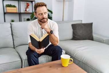 Orta yaşlı İspanyol adam evde kitap okuyor.