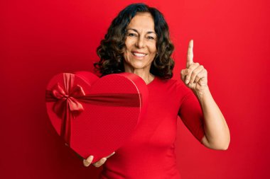 Orta yaşlı İspanyol kadının elinde sevgililer günü hediyesi var. Bir fikir ya da soruyla şaşırmış. Mutlu bir yüzle işaret ediyor. 