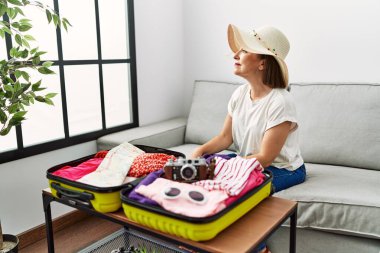 Güzel, orta yaşlı, İspanyol bir kadın valize yazlık giysiler koyuyor. Yan tarafa bakıyor, rahat poz veriyor, kendine güvenen bir gülümsemesi var.. 