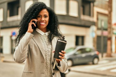 Orta yaşlı Afro-Amerikan iş kadını akıllı telefondan konuşuyor ve şehirde kahve içiyor..