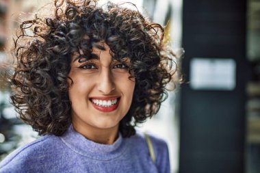 Orta Doğu 'lu genç bir kadın sokakta kendinden emin gülümsüyor.