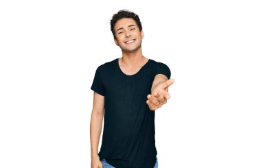 Young handsome man wearing casual black t shirt smiling friendly offering handshake as greeting and welcoming. successful business. 