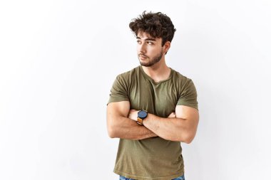 Hispanic man standing over isolated white background looking to the side with arms crossed convinced and confident 