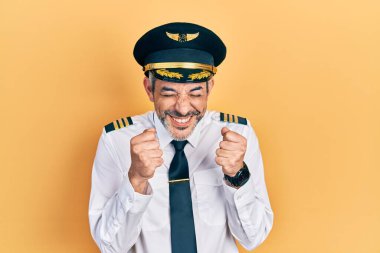 Handsome middle age man with grey hair wearing airplane pilot uniform excited for success with arms raised and eyes closed celebrating victory smiling. winner concept. 