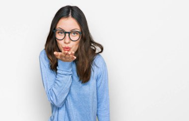 Gündelik giysiler ve gözlük takan genç ve güzel bir kadın kameraya bakıp havada bir öpücük savuruyor ve sevimli ve seksi oluyor. aşk ifadesi. 