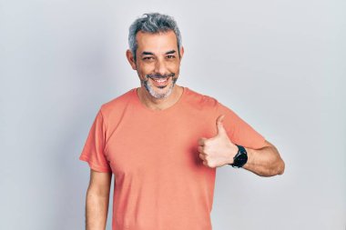 Handsome middle age man with grey hair wearing casual t shirt doing happy thumbs up gesture with hand. approving expression looking at the camera showing success. 