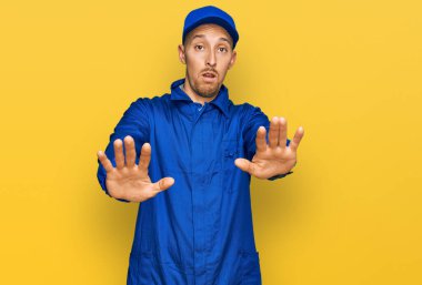 Bald man with beard wearing builder jumpsuit uniform doing stop gesture with hands palms, angry and frustration expression 