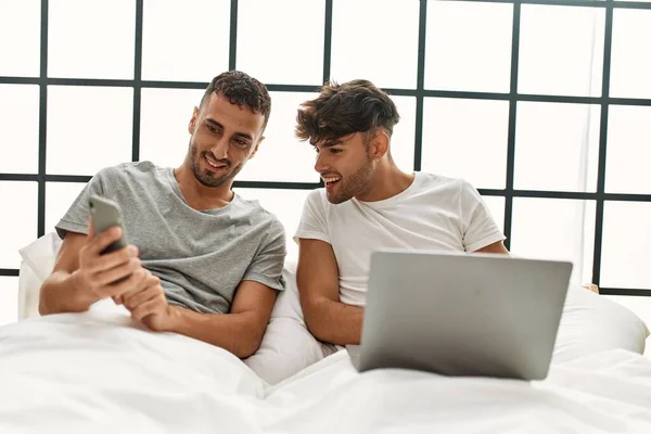 Dois Homens Hispânicos Casal Usando Laptop Smartphone Sentado Cama Quarto — Fotografia de Stock