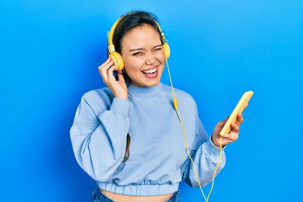 Young Hispanic Girl Using Smartphone Headphones Winking Looking Camera Sexy — Stockfoto