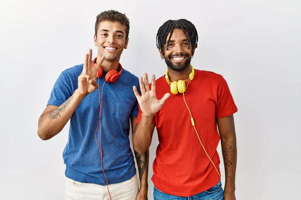 自信を持って幸せな笑みを浮かべている間 8番目の指で見せ 指差すヘッドフォンを身に着けている隔離された背景の上に立っている若いヒスパニック系の兄弟 — ストック写真